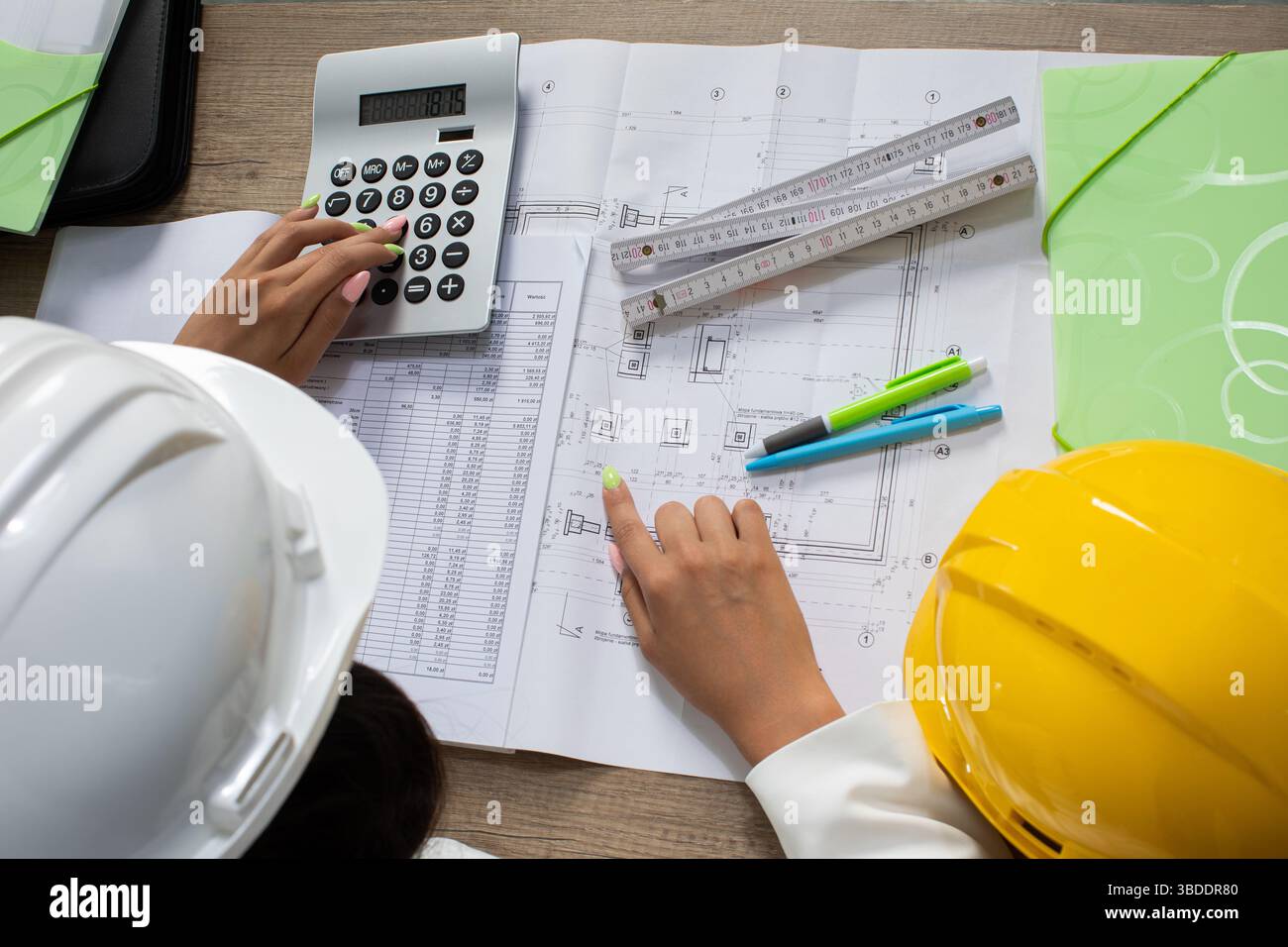 Engineers are Collaborating on Construction Plans while Utilizing Various Calculating Tools Stock Photo
