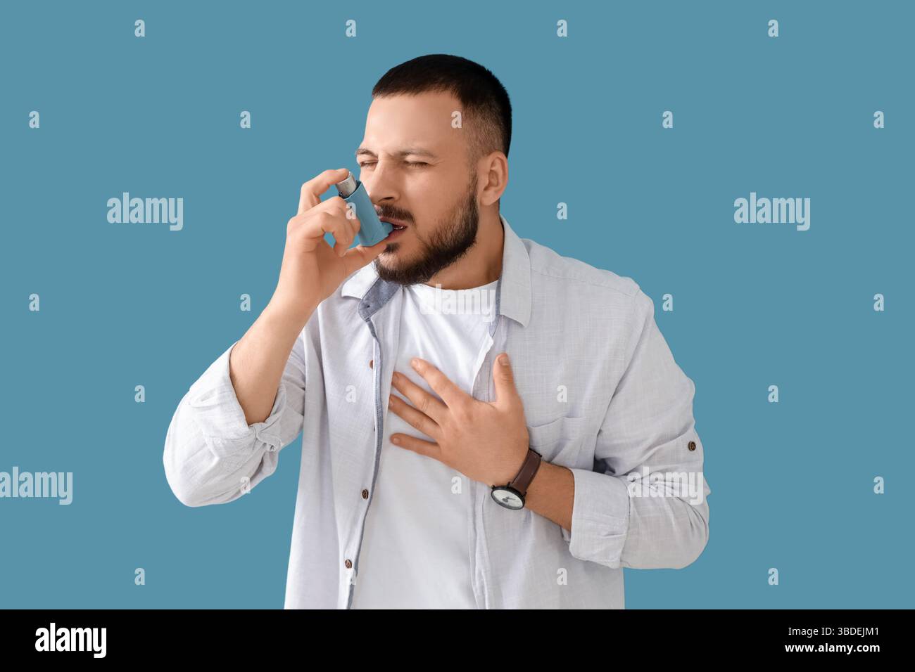 Young man with asthma attack using inhaler on blue background Stock Photo