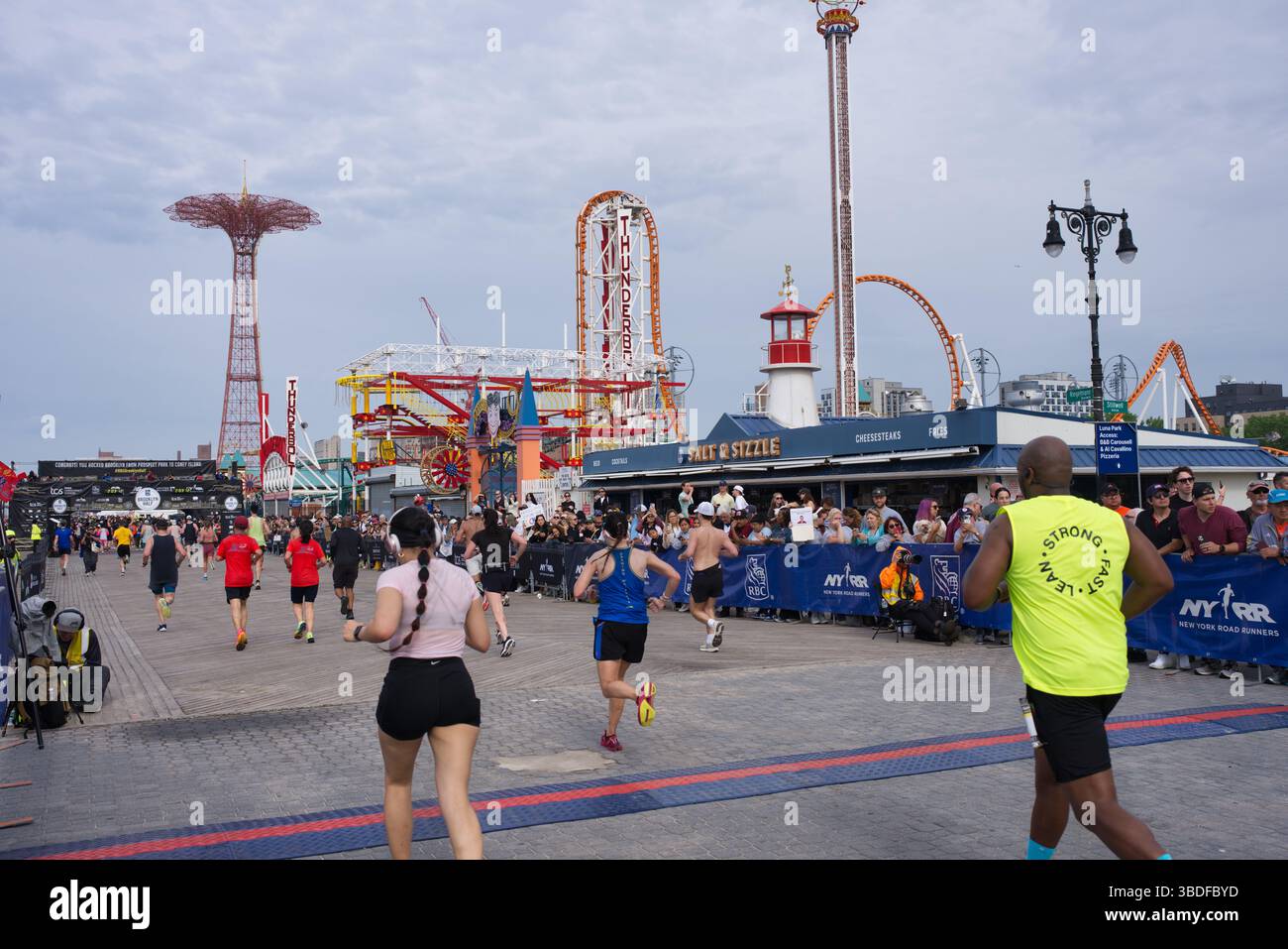 Picture of Runners participate in a road race along a boardwalk, with Coney Island ...