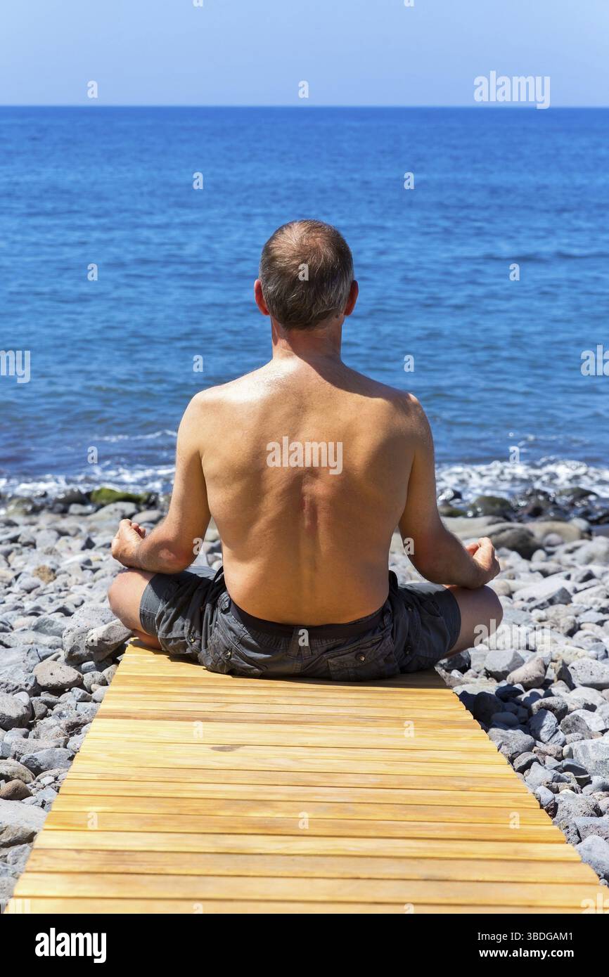 Middle aged man meditating at coast and ocean Stock Photo