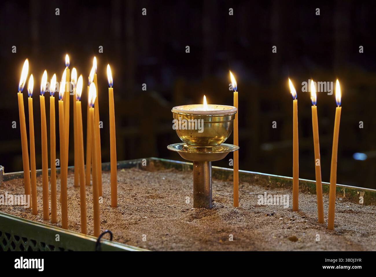 Close-up of burning candles in a sand container in dark surroundings ...