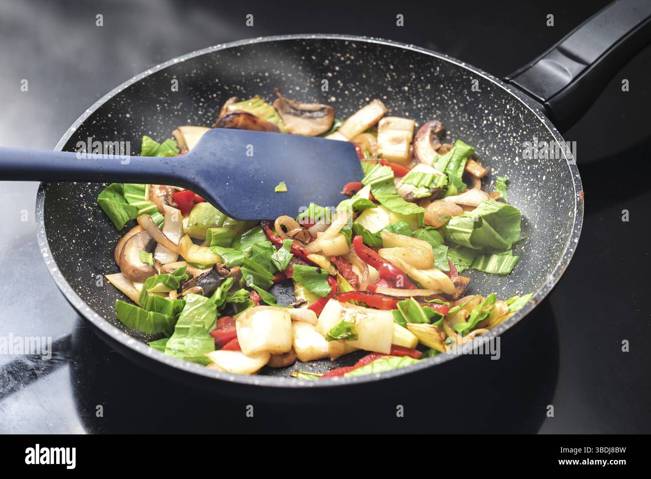 Stir-fried vegetables steaming in a frying pan, healthy vegetarian cooking with ingredients like bell pepper, mushroom, onions and pak choi or Chinese Stock Photo