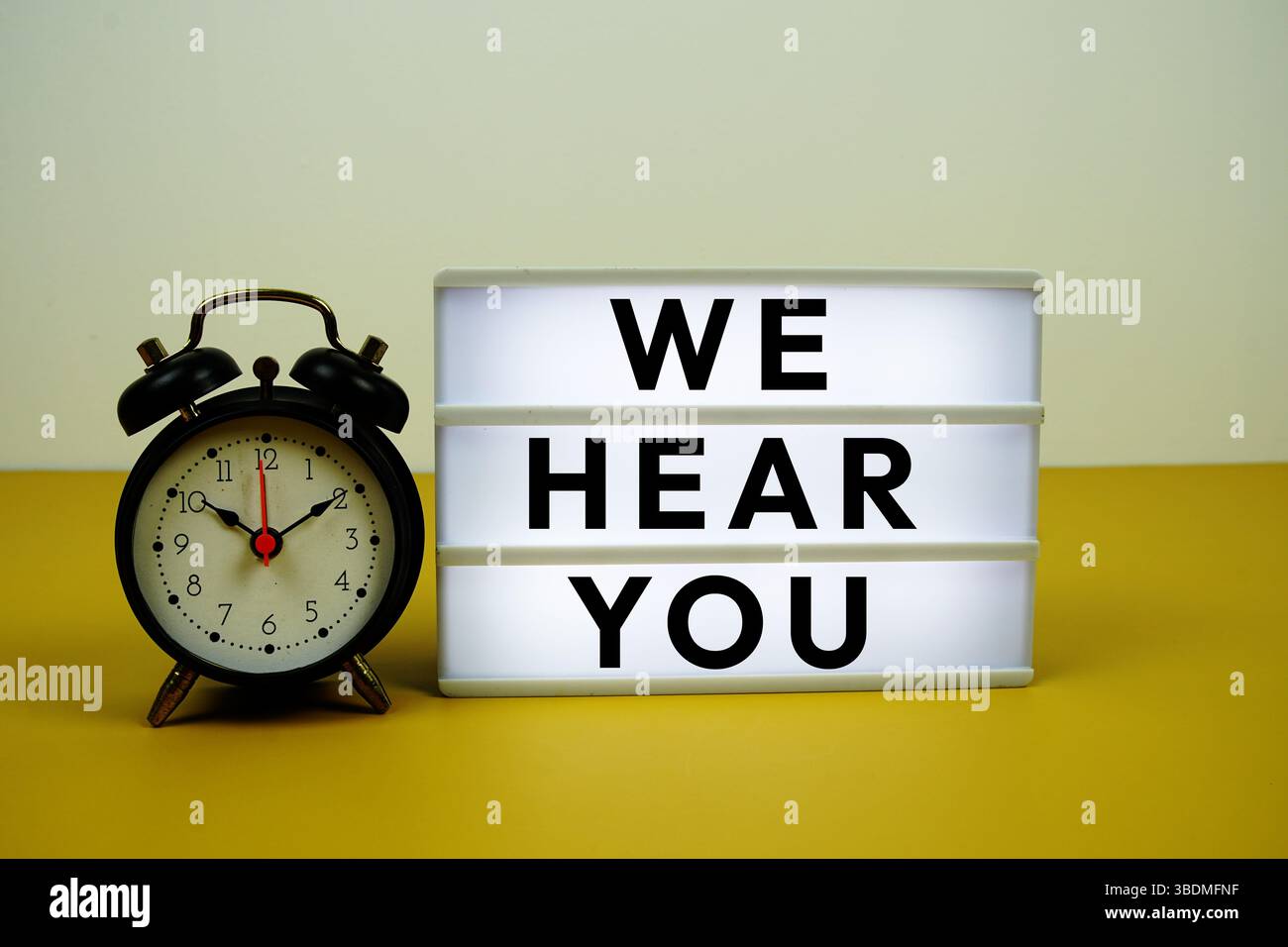 We Hear You text on LED lightbox with alarm clock on yellow background Stock Photo