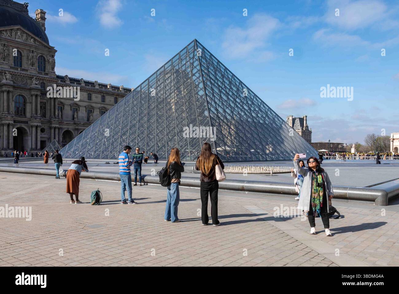 Tourists taking pictures with and of the Louvre Museum glass pyramid skylight in Cour Napoléon in Paris, France Stock Photo