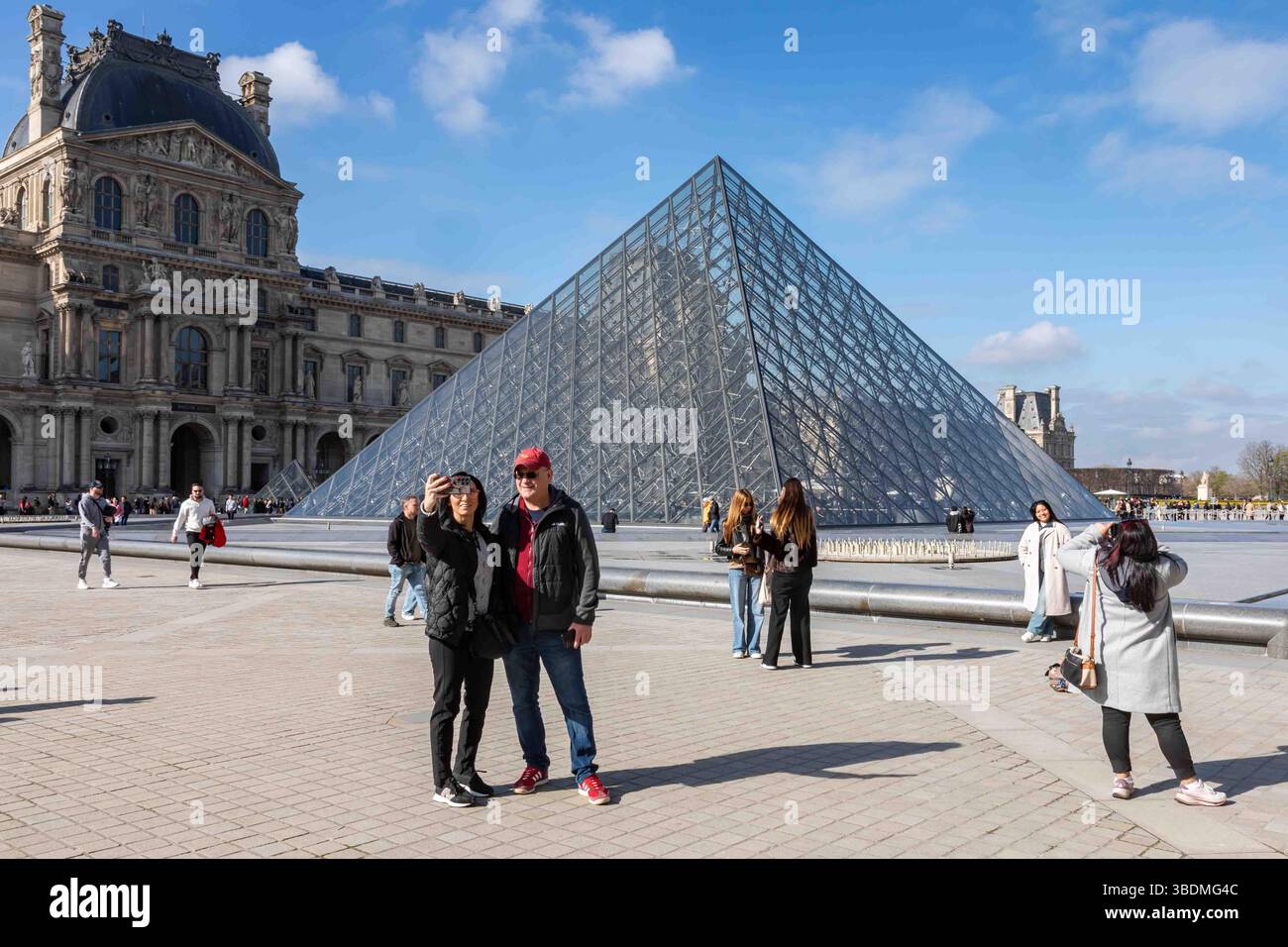Tourists on Napoleon Courtyard taking selfies and pictures in front of Louvre Museum glass pyramid skylight in Paris, France Stock Photo