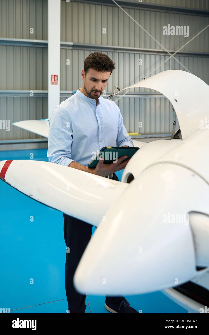 Aircraft mechanic using digital tablet while inspecting airplane in hangar Stock Photo