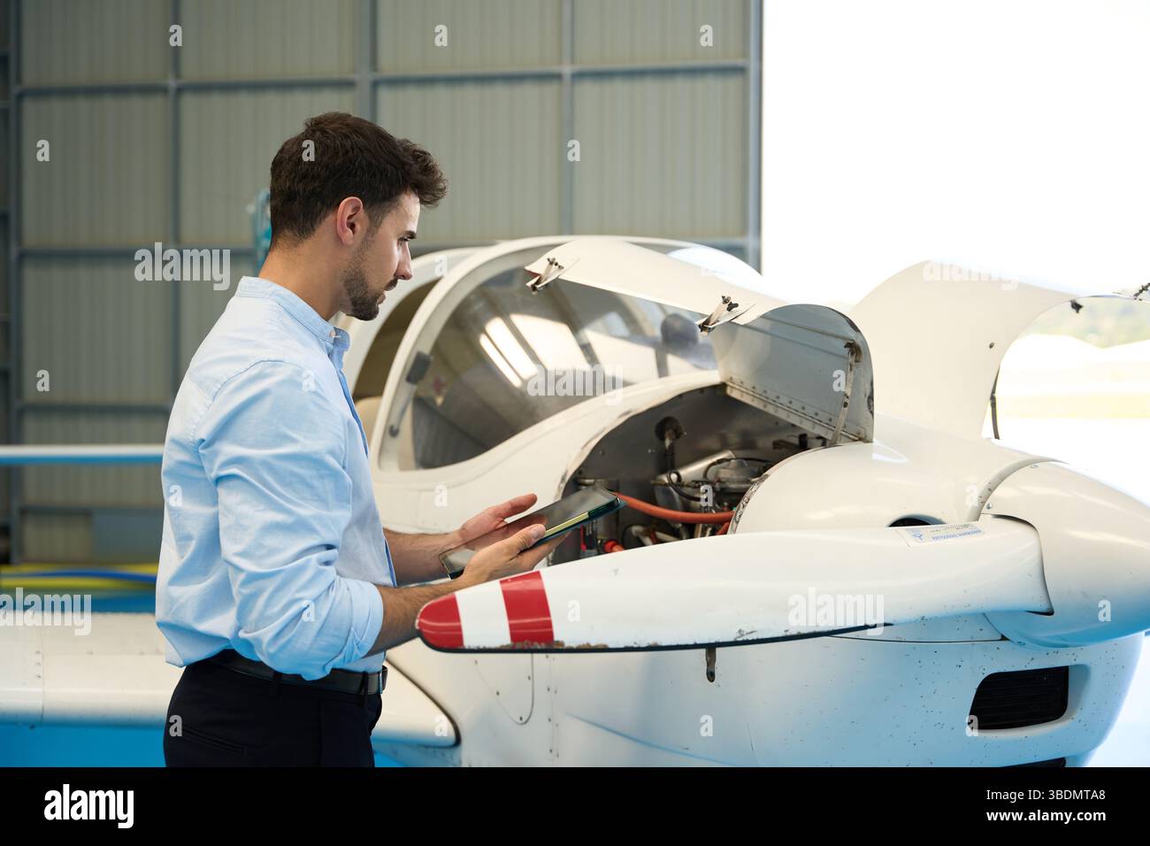Aircraft mechanic using digital tablet performing maintenance check on small airplane engine Stock Photo