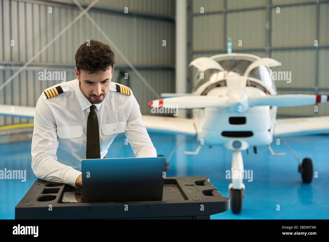 Pilot using laptop in hangar with small airplane Stock Photo