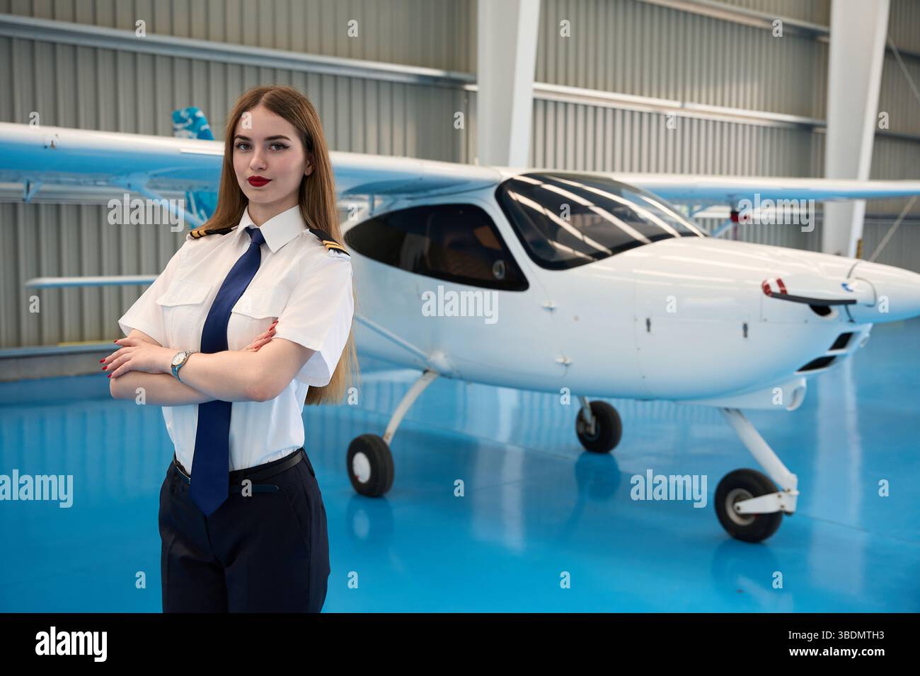 Confident female pilot posing in hangar with small airplane Stock Photo ...