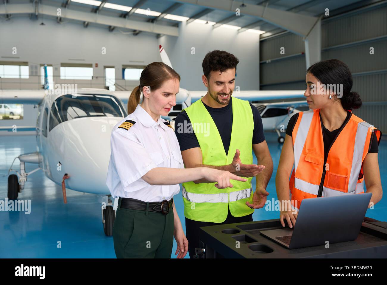 Pilot and mechanics discussing maintenance using laptop in hangar Stock Photo