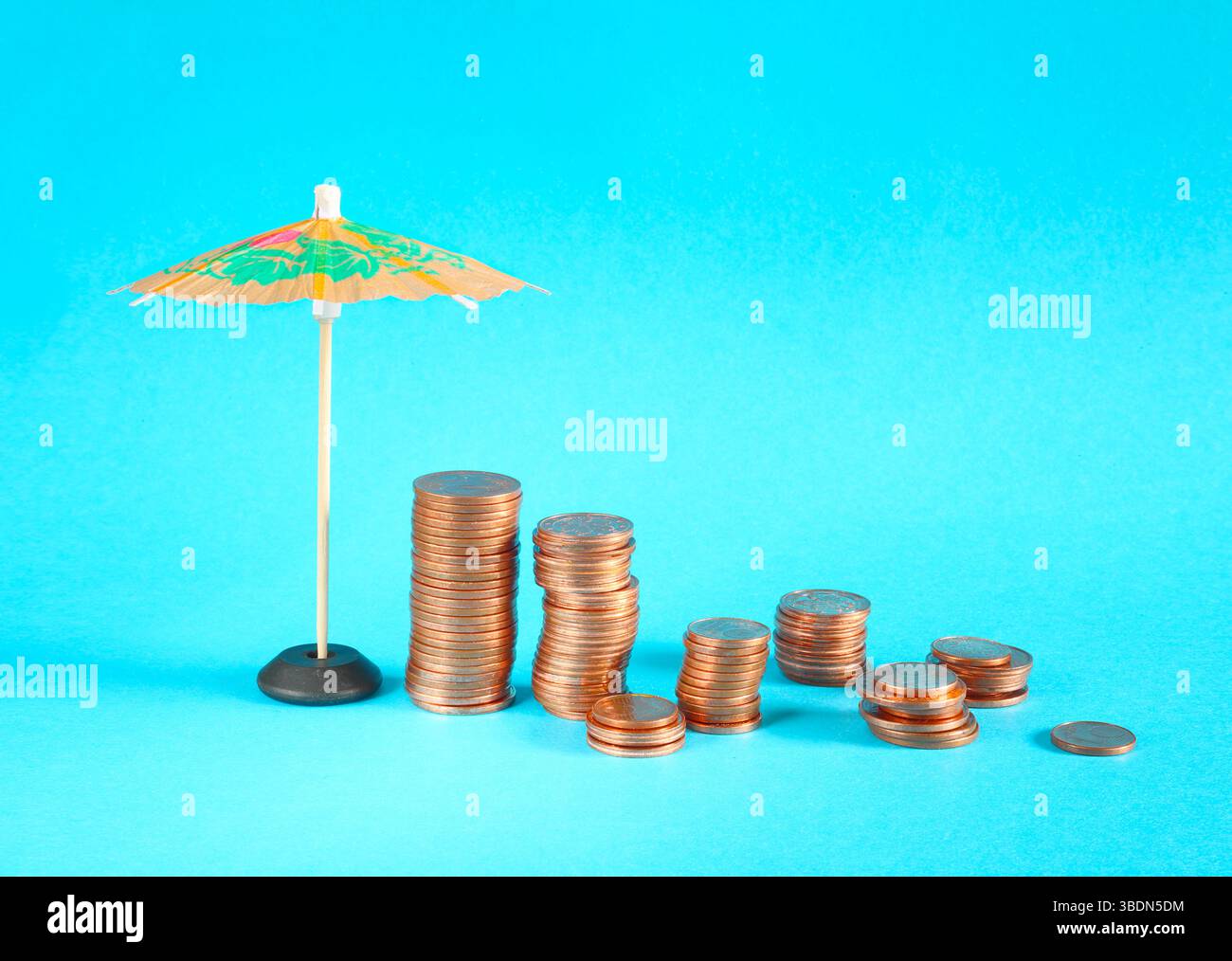 Stacked coins are protected by umbrella on blue background with copy space. Assets wealth, money saving or money investment protection Stock Photo