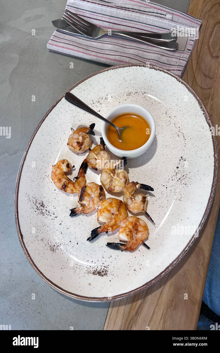 Baked shrimp on a skewer on a white plate with sauce. Restaurant meal, lifestyle. Vertical photo. - Smartphone Captured Stock Image