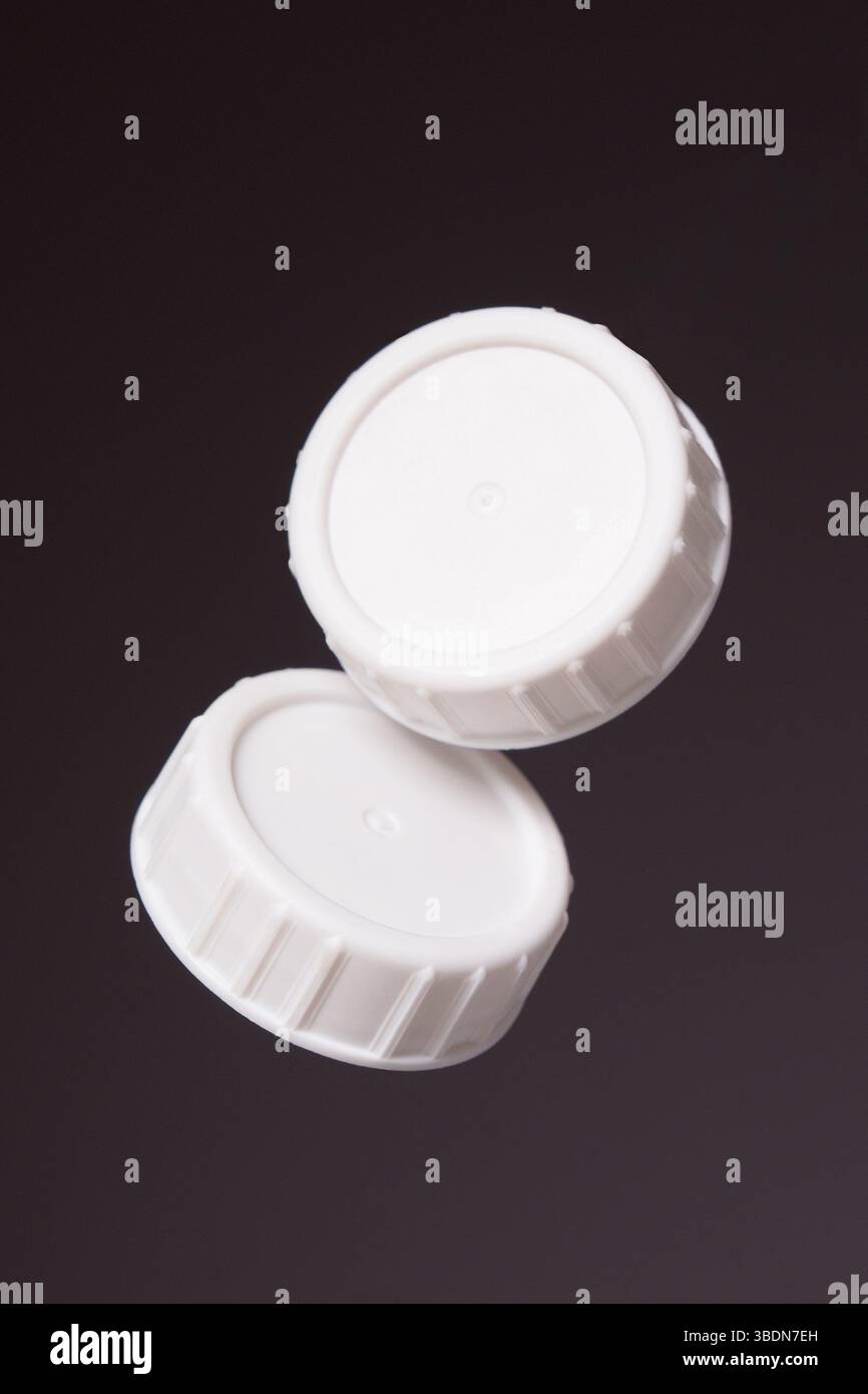 Two white plastic bottle caps on a black background. Close up. Stock Photo