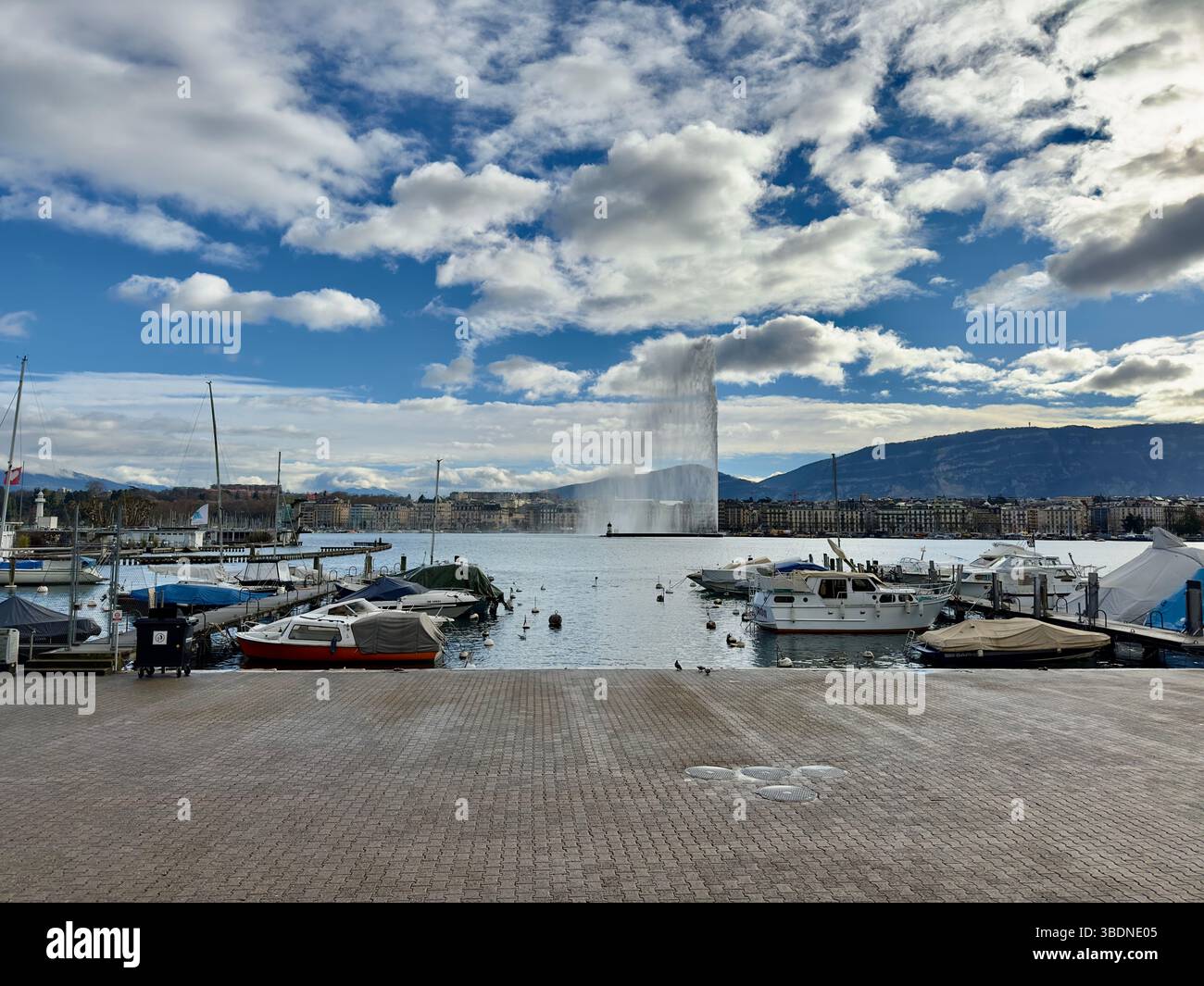 The iconic Jet d'Eau fountain in Geneva sprays high above the serene lake against a cloudy sky. - Smartphone Captured Stock Image