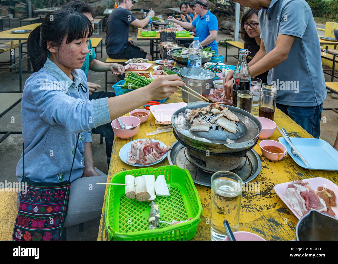 Thai woman cooking fish on a charcoal hot pot at a buffet style outdoor ...