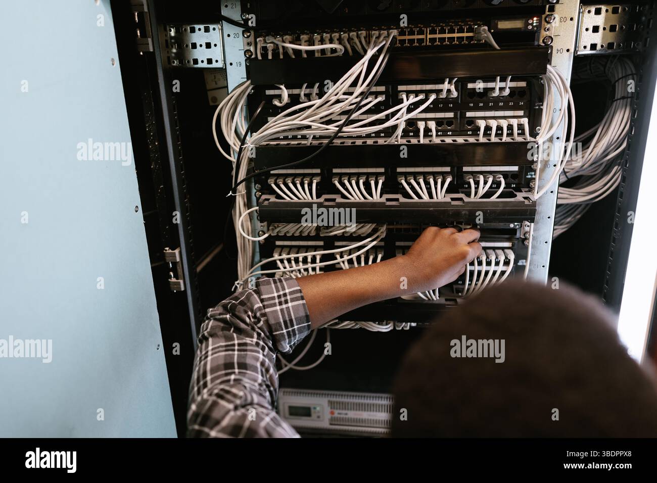 Technician managing network cables in a server room during the afternoon hours Stock Photo