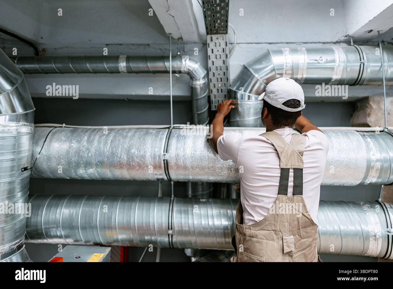 Skilled worker installing metal ductwork in a commercial building during a maintenance project Stock Photo
