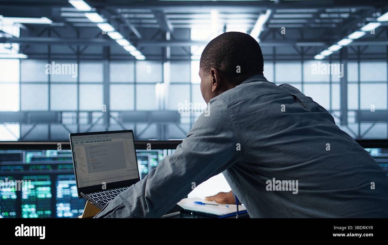 Technician coding on laptop in data center, managing server virtualization, finetuning network protocols. Server farm employee programming on notebook, enforcing advanced security measures, camera B Stock Photo