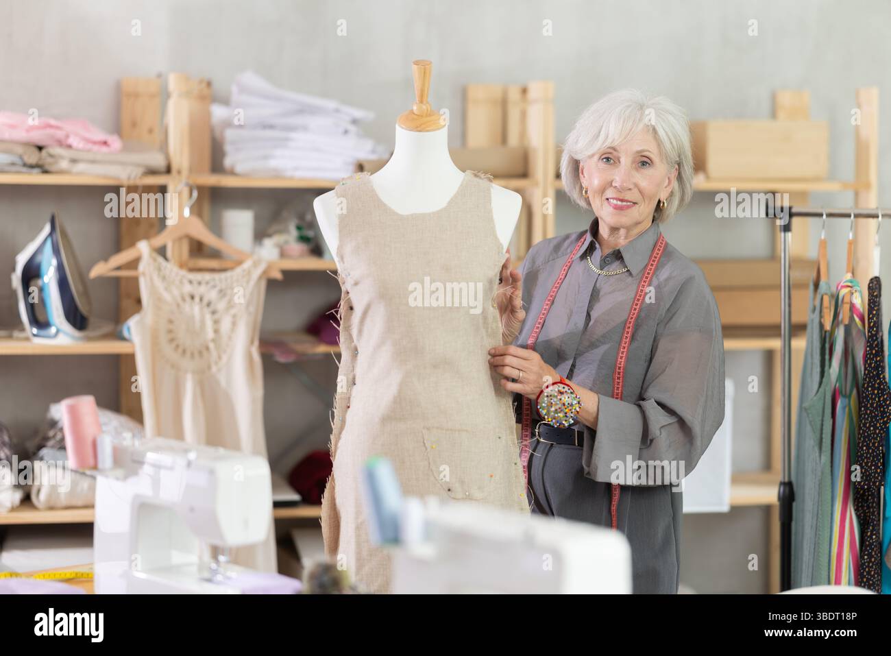 Positive mature female dressmaker working with mannequin in sewing ...