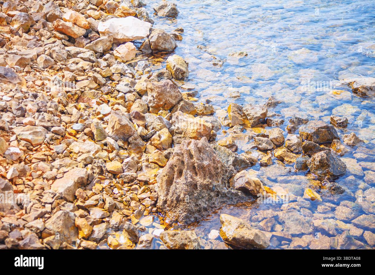Rocky shoreline with various sizes and shapes of stones extending into ...