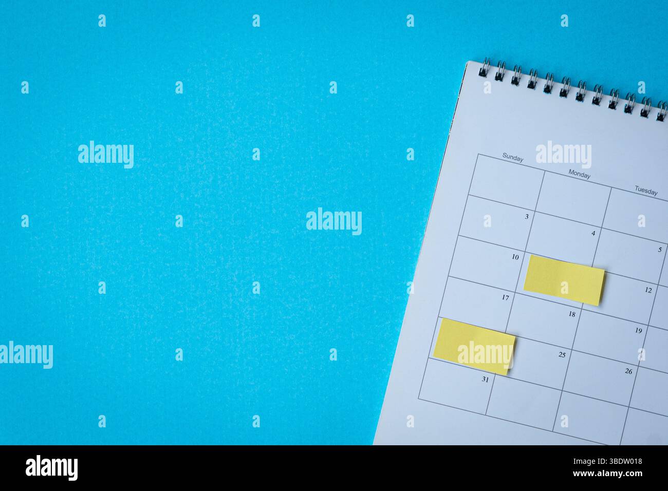 Calendar page with yellow adhesive notes. On top of blue surface, high angle view. Copy space. Stock Photo