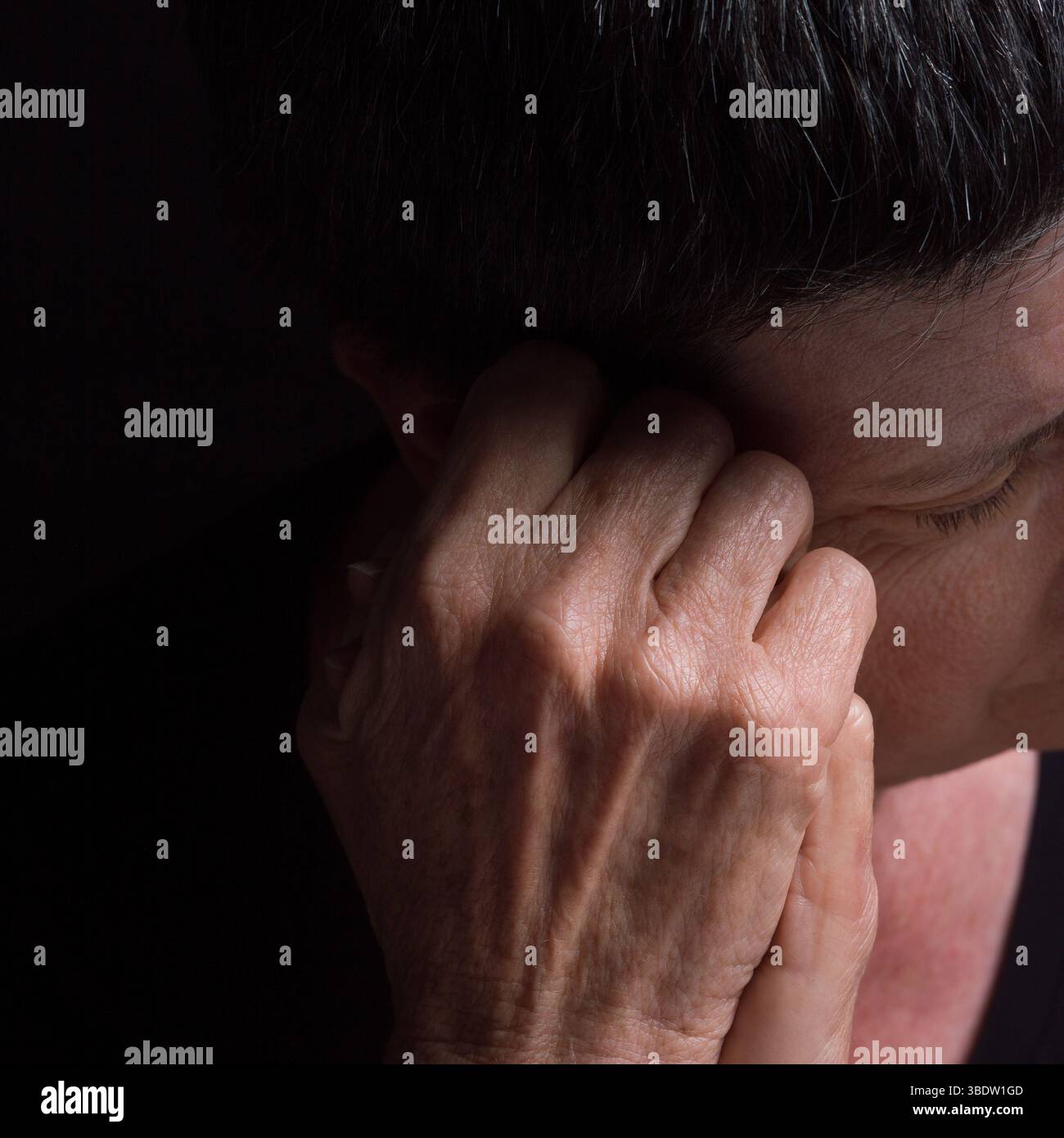 A woman with short hair rests her head on her hand, conveying deep contemplation and introspection in low lighting Stock Photo