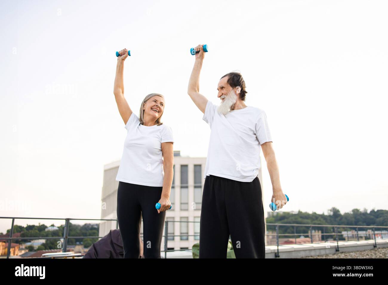 Happy senior couple exercising outdoors using light dumbbells on sunny day Stock Photo