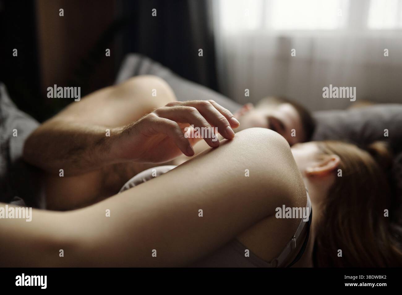 Intimate tender embrace in a cozy bedroom, soft morning light filtering through curtains, warm loving atmosphere of connection