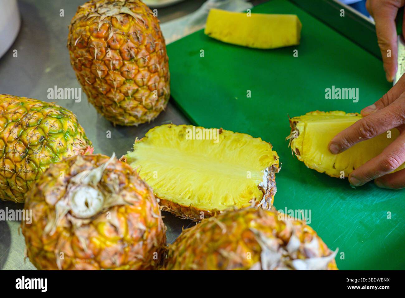 hands preparing fresh pineapple on green cutting board in kitchen Stock Photo