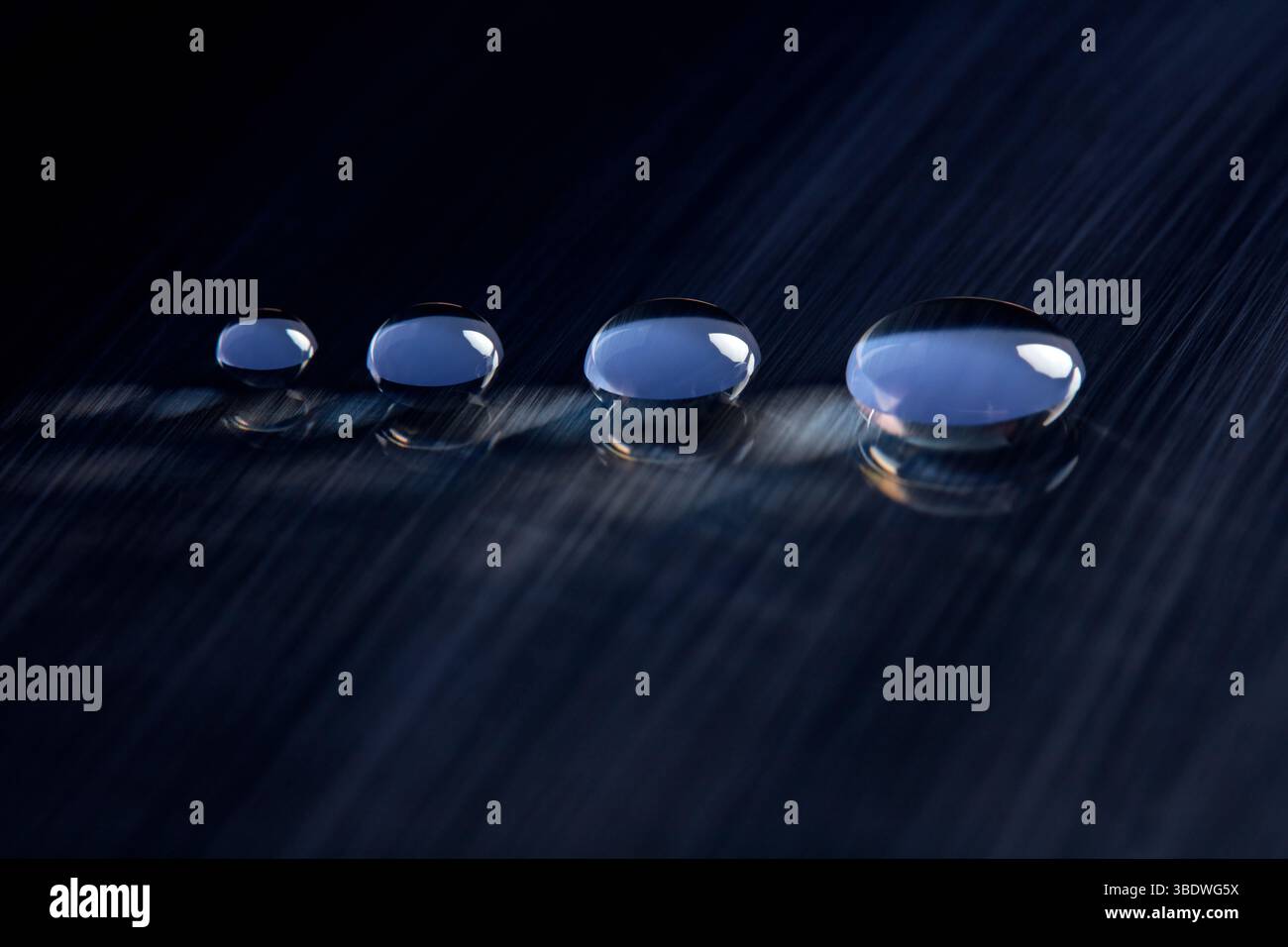 Four round water droplets on a dark blue, textured surface. V3 Stock Photo