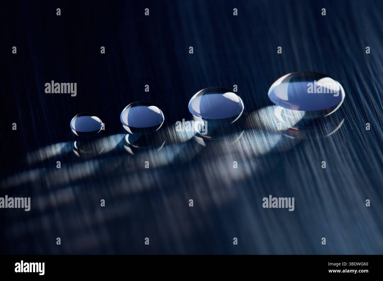 Four round water droplets on a dark blue, textured surface. V2 Stock Photo