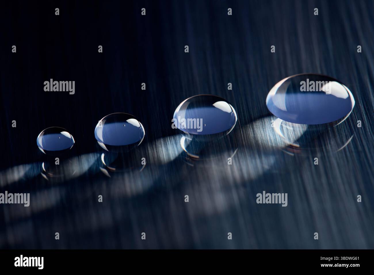 Four round water droplets on a dark blue, textured surface. Stock Photo