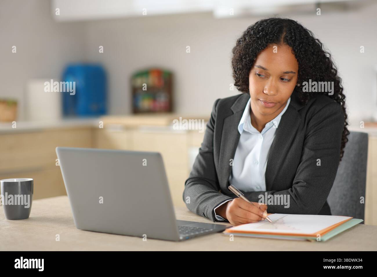 Black executive working online taking notes in a notebook and checking laptop at home Stock Photo