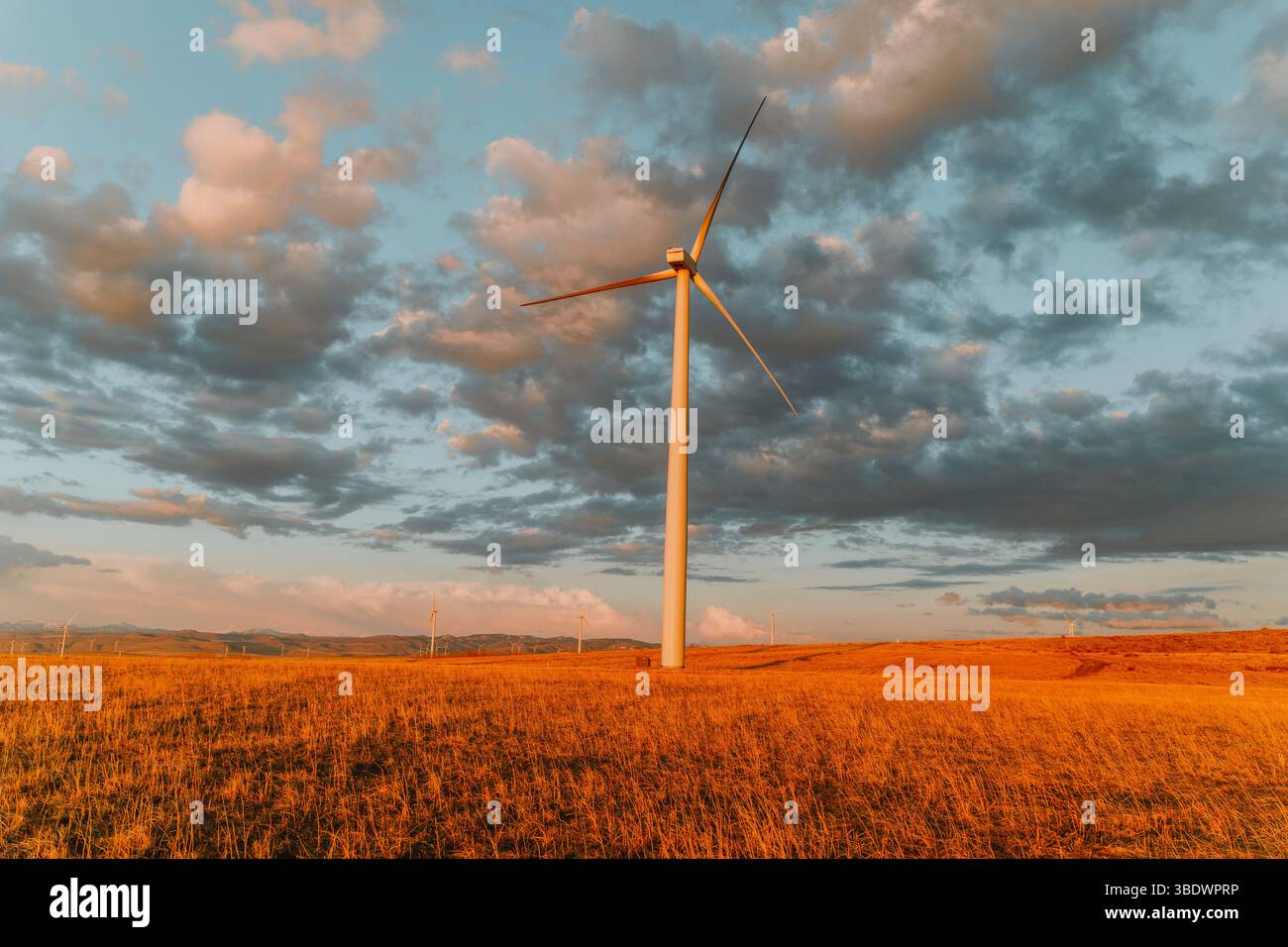 Single wind turbine stands tall against moody evening sky. Stock Photo