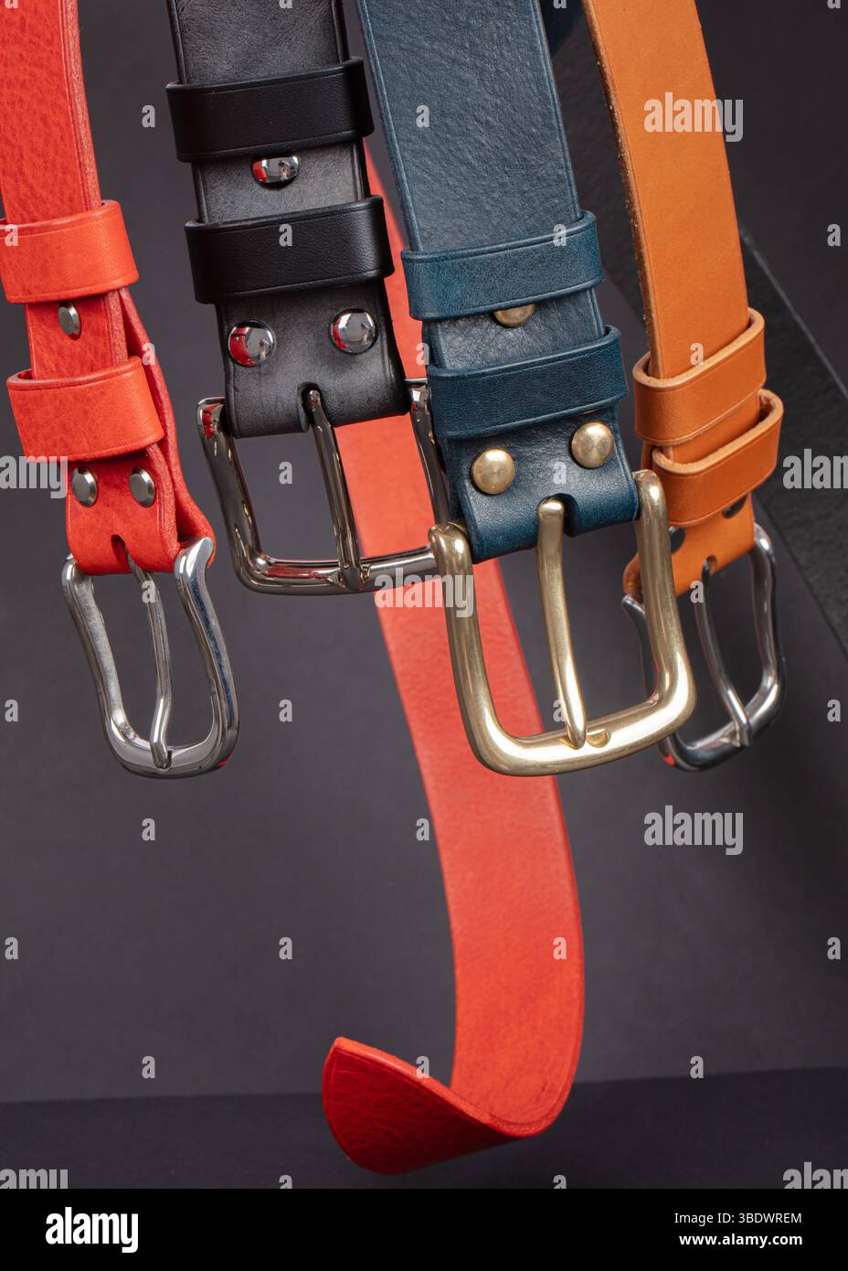 Various leather belts with metal buckles close-up on dark grey background. Stock Photo