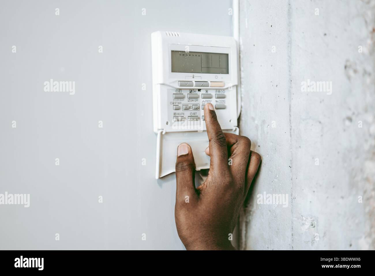 Person interacting with a security panel on a wall in a modern setting during daytime Stock Photo
