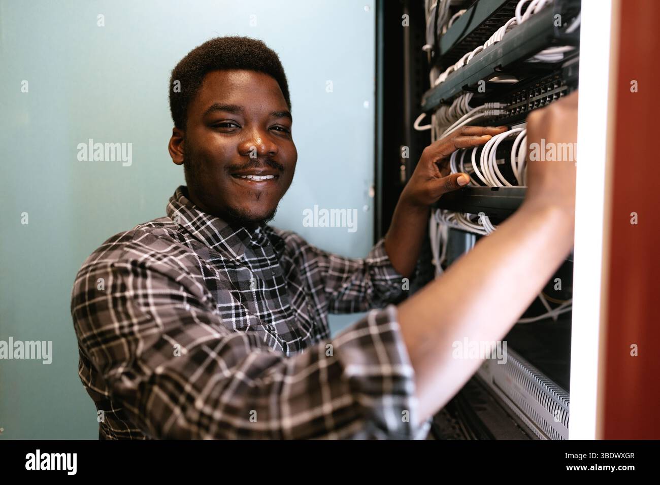 Technician organizes network cables in server room during daytime, ensuring efficient connectivity Stock Photo