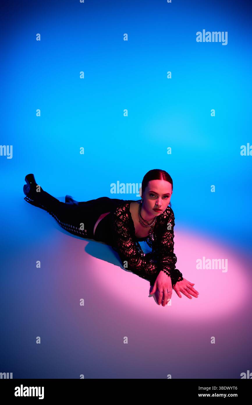 A stylish young woman poses gracefully on the studio floor, illuminated ...