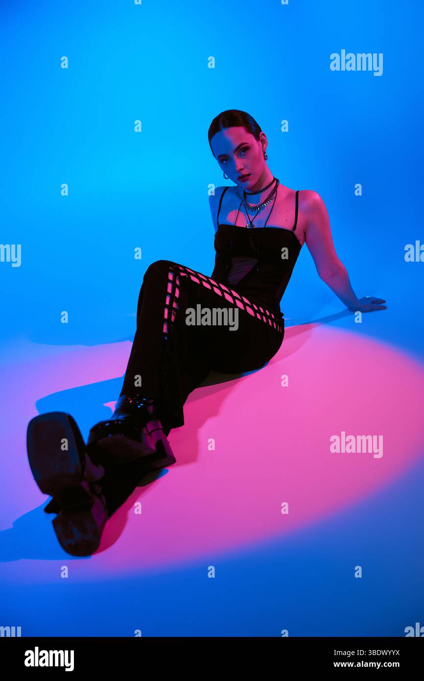 Stylish young woman poses confidently in a chic outfit, illuminated by colorful lighting. Stock Photo