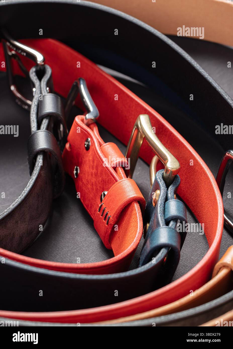 Various leather belts with metal buckles close-up on dark grey background. Stock Photo