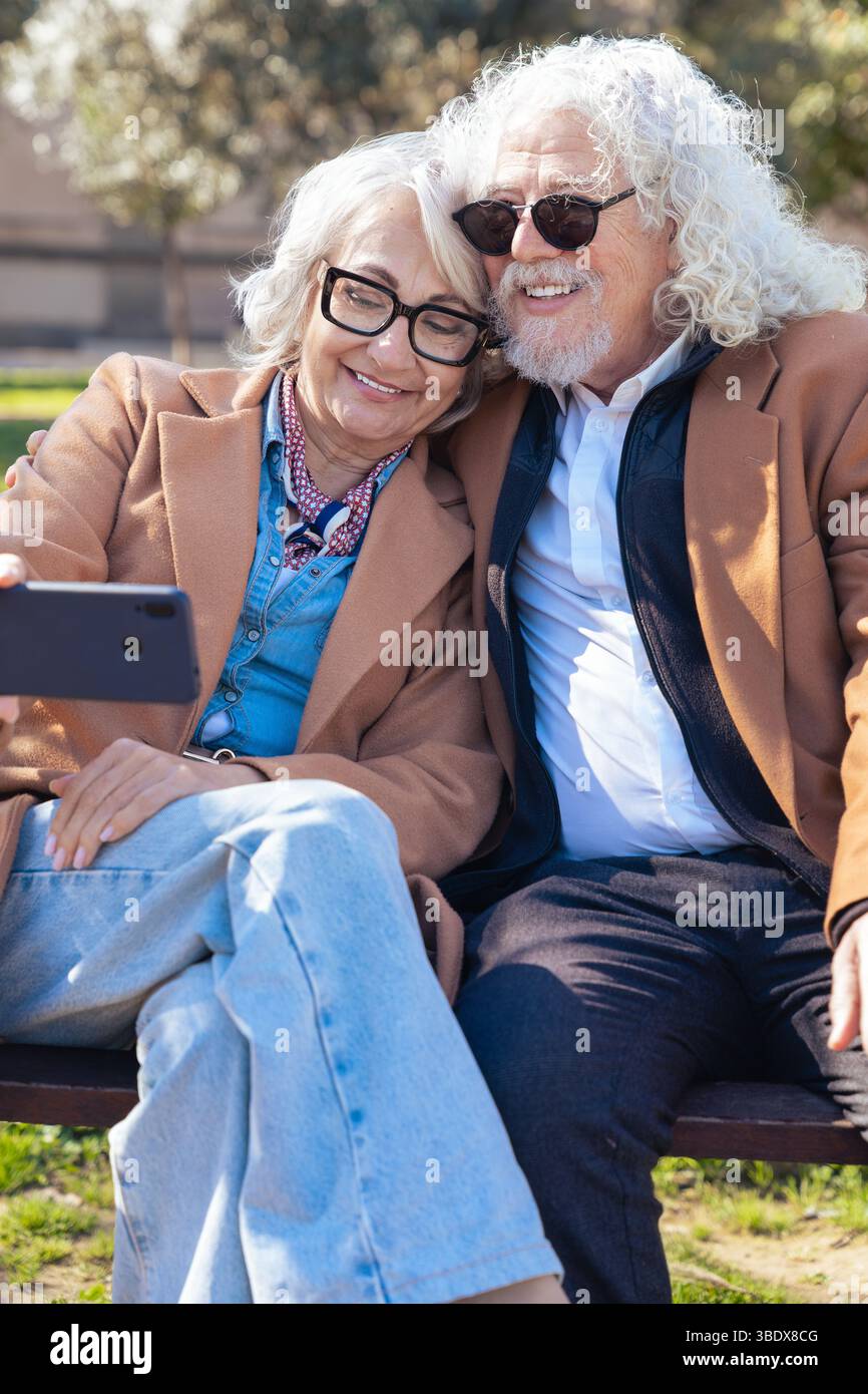 Senior couple taking selfie outdoors with smartphone, smiling and sunglasses Stock Photo