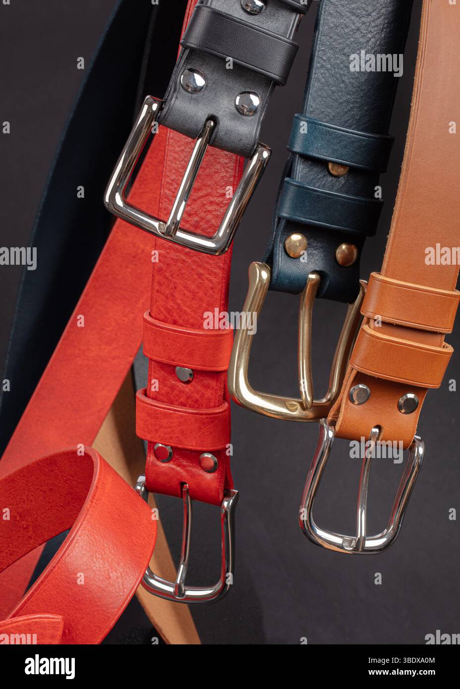 Various leather belts with metal buckles close-up on dark grey background. Stock Photo