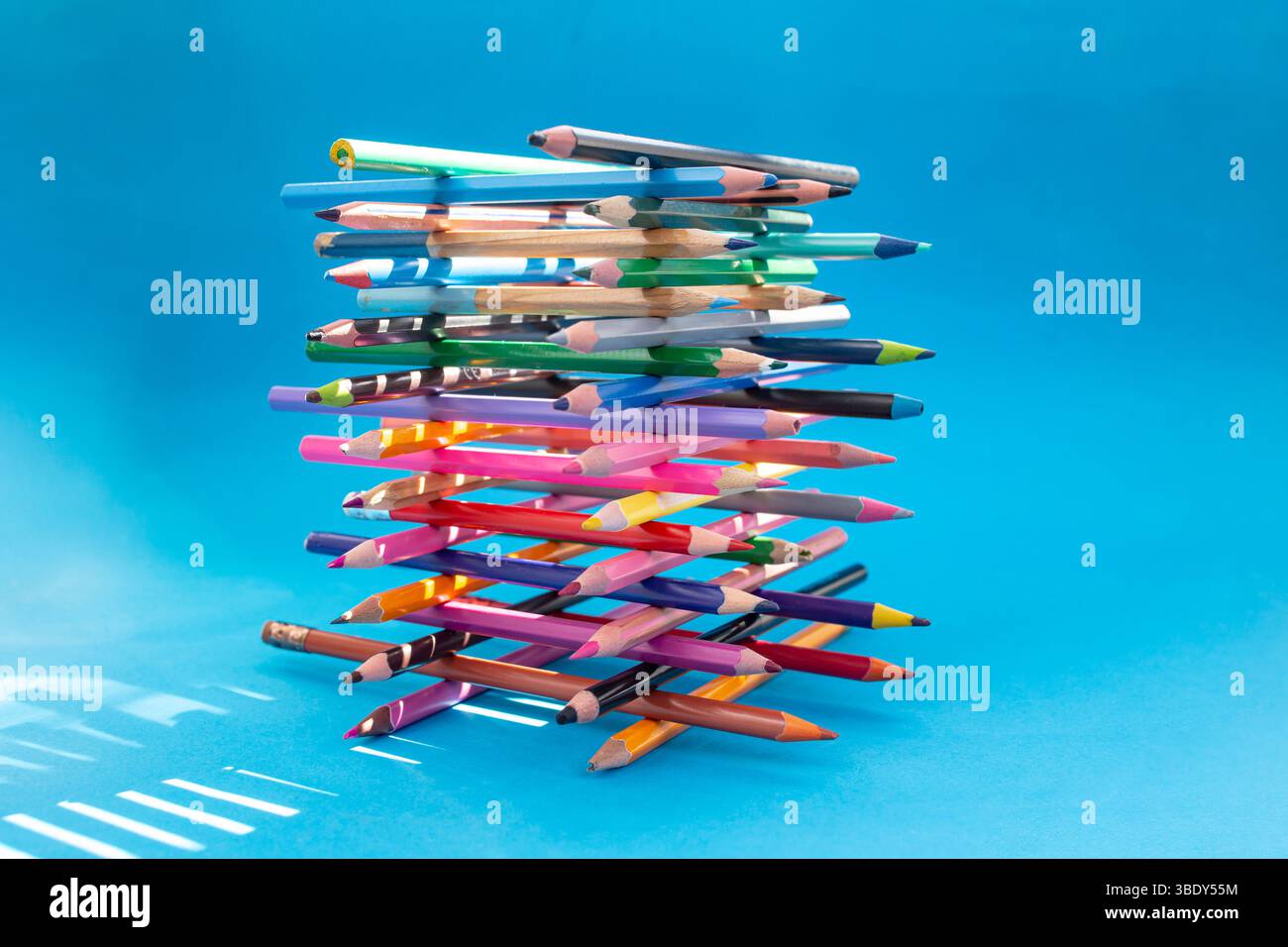 Stacked colored crayons stacked in the shape of a high tower illuminated with sun light on blue Stock Photo