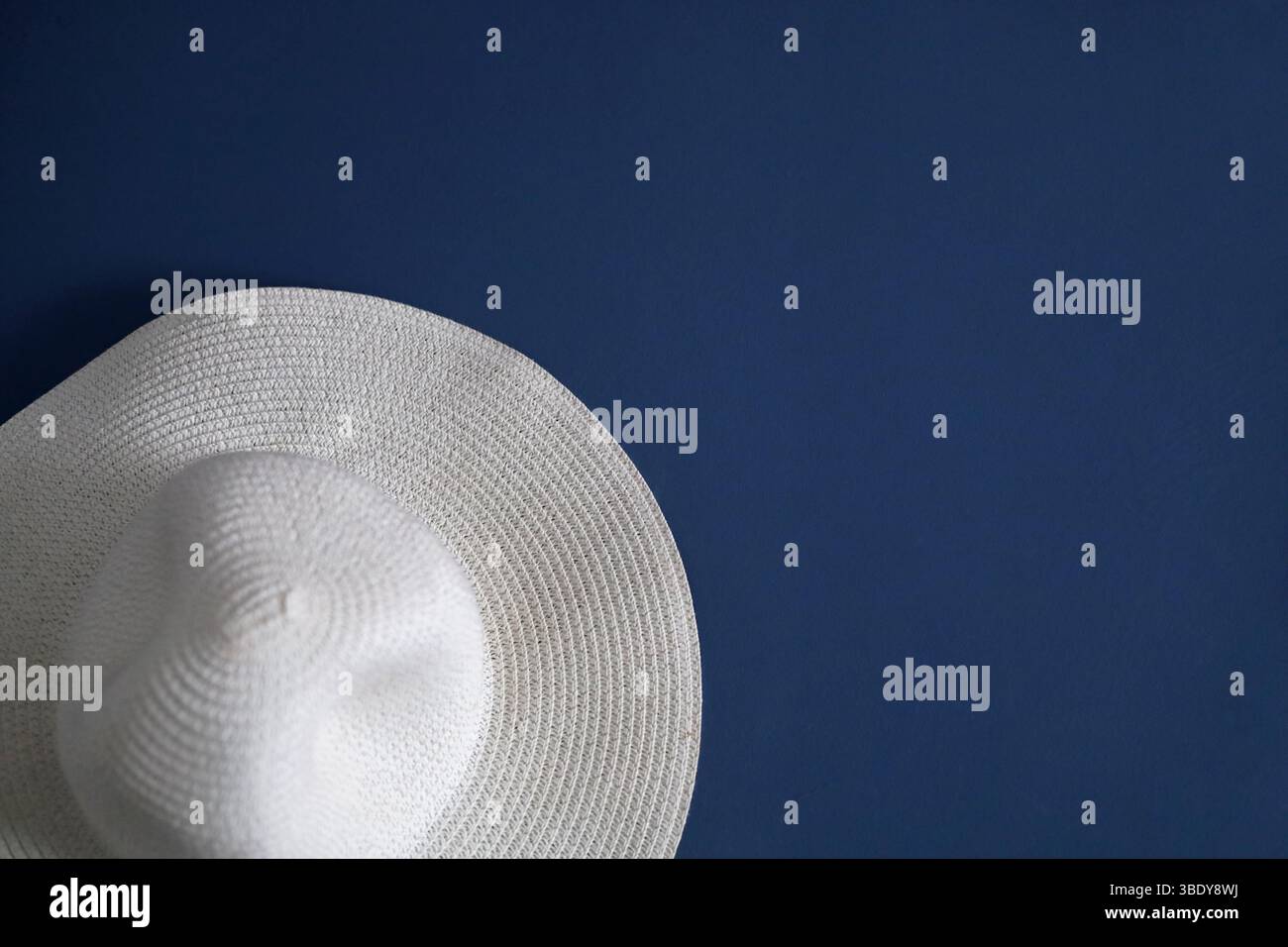 Elegant, white, braided hat hanging on the blue wall Stock Photo