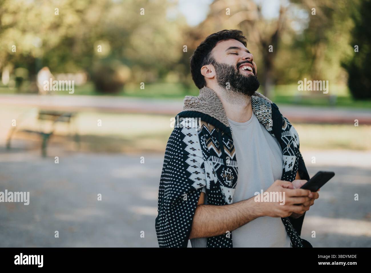 Man laughing while using smart phone outdoors in a sunny park Stock Photo