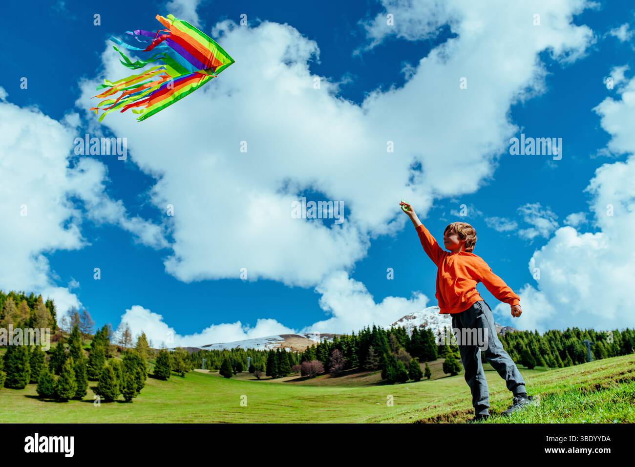 Happy boy with kite on green field on mountains background Stock Photo