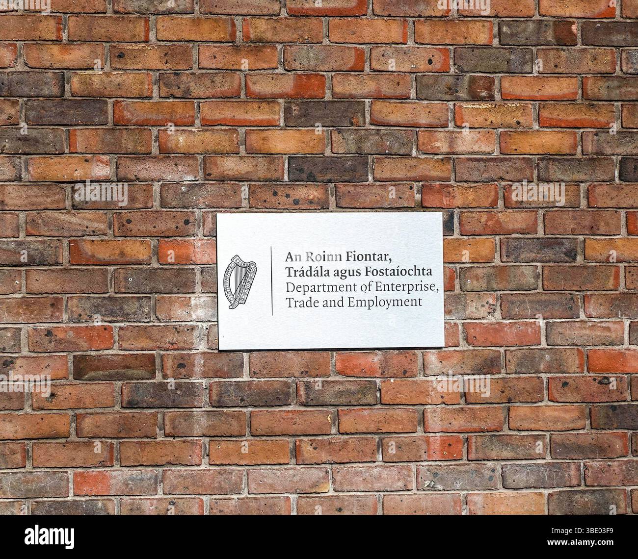 Sign for the Department of Enterprise, Trade and Employment on a red brick wall at Earlsfort Terrace, Dublin, Ireland. Irish and English text visible. Stock Photo