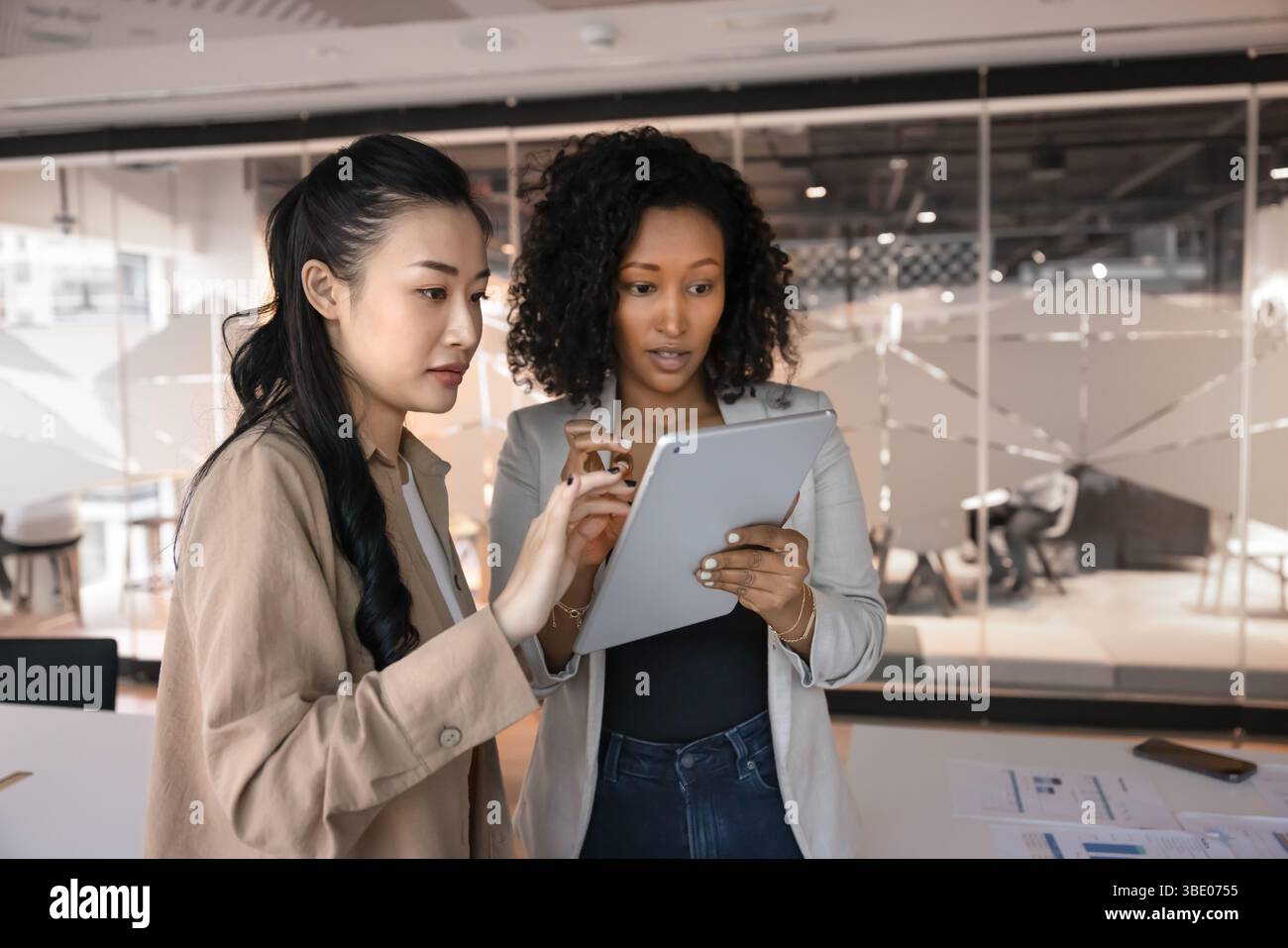 Two young multiethnic women workmates using tablet standing in workspace Stock Photo
