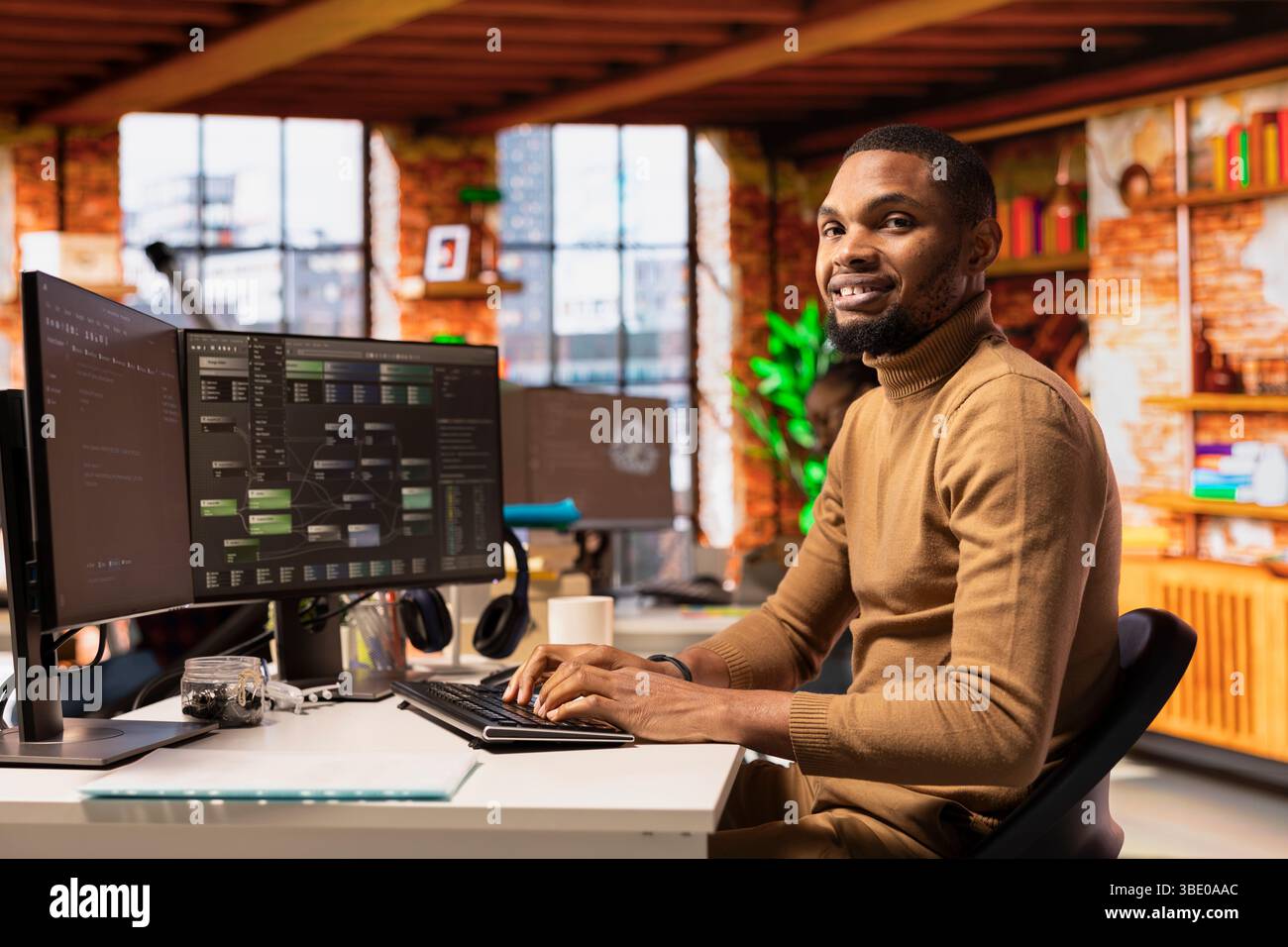 Portrait of cheerful IT technician using PC in innovative startup office and programming languages to build applications. Joyous software development agency IT expert optimizing code on computer Stock Photo