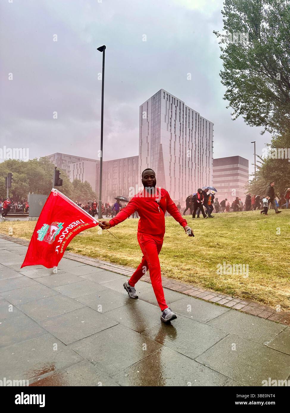 Man dressed in red waves a large red flag while walking along Hunter Street during Liverpool’s football victory parade, Liverpool, UK, 26 May 2025. - Smartphone Captured Stock Image